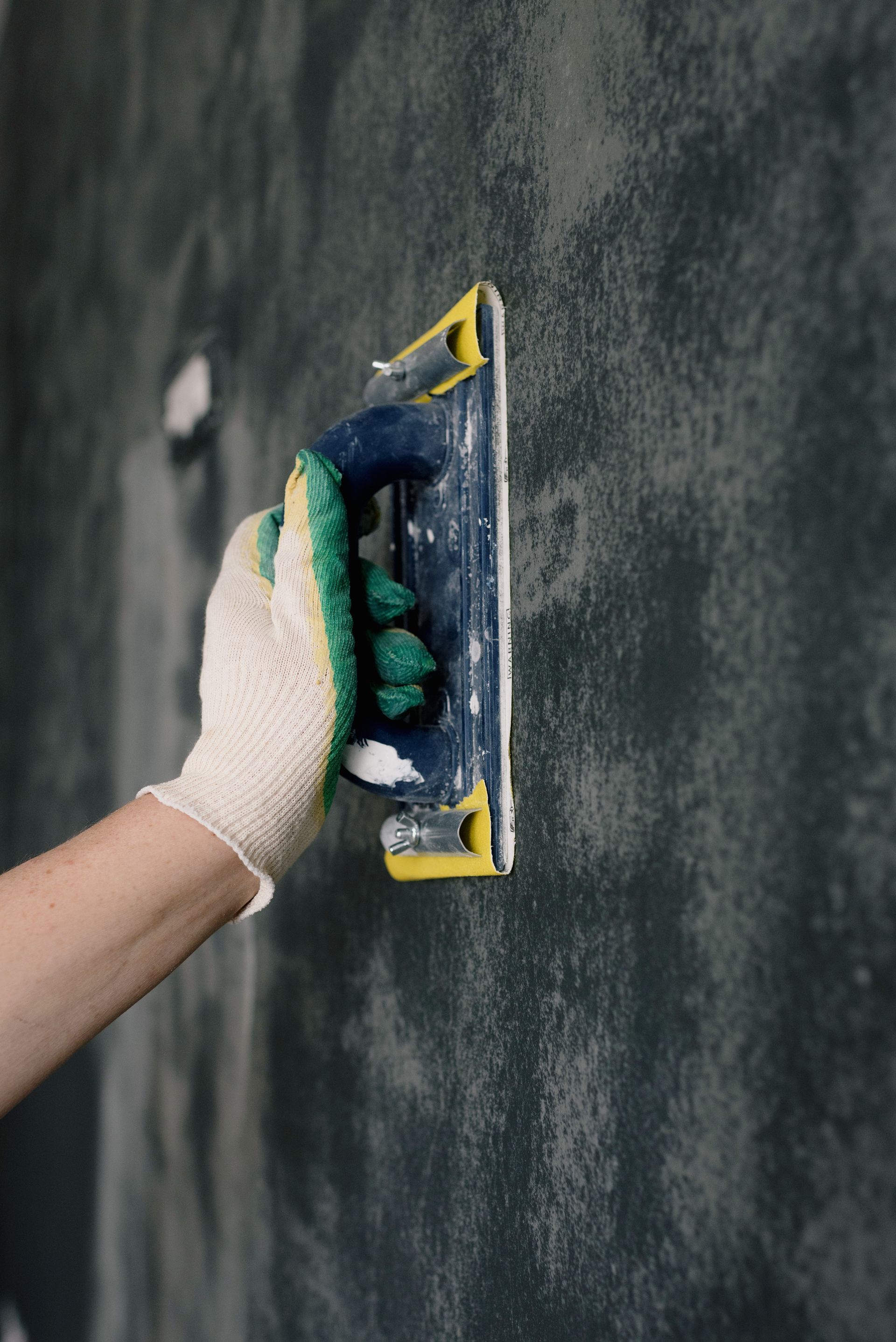 Hand sanding a wall during preparation for property maintenance work