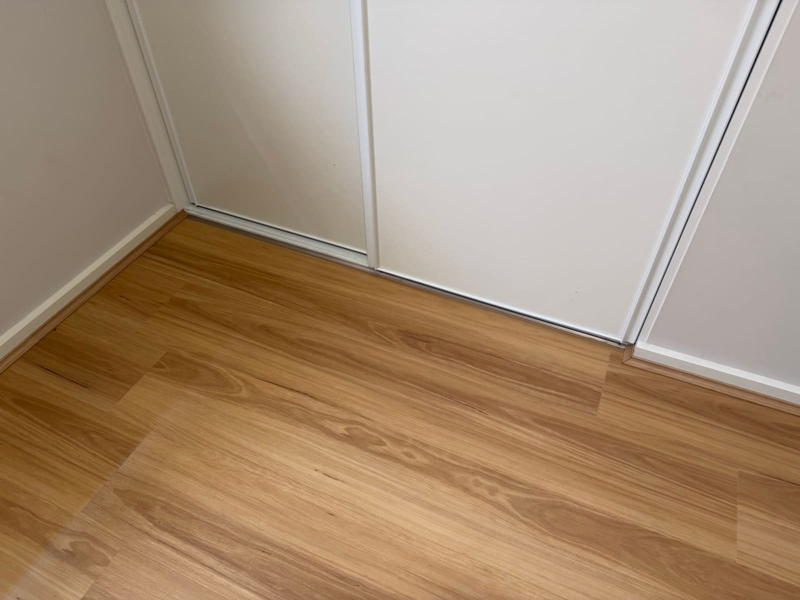 Timber-look flooring finished with matching scotia trim along a white sliding wardrobe