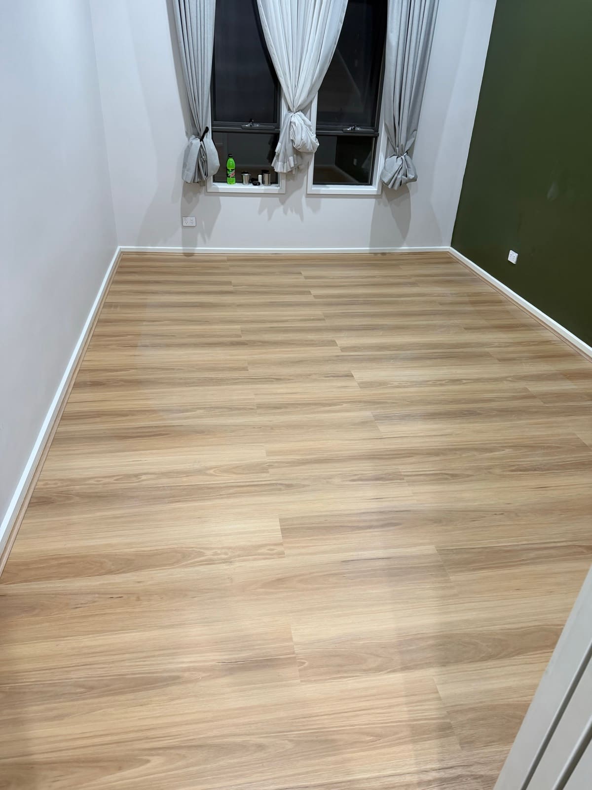 Light oak laminate flooring with white skirting and a green feature wall in an Adelaide home